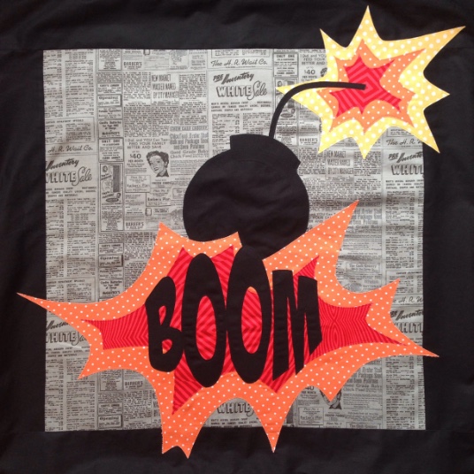 A patchwork applique block with a cartoon bomb exploding and the word BOOM