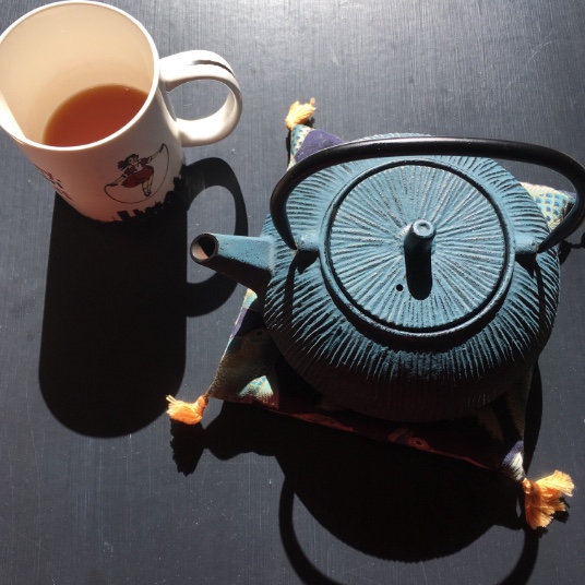 A Mug filled with tea and a blue cast iron teapot for one